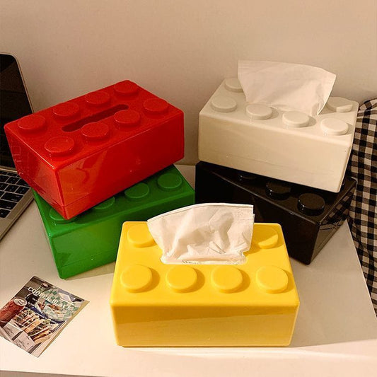 Four colorful brick-shaped tissue boxes on a surface with a magazine.