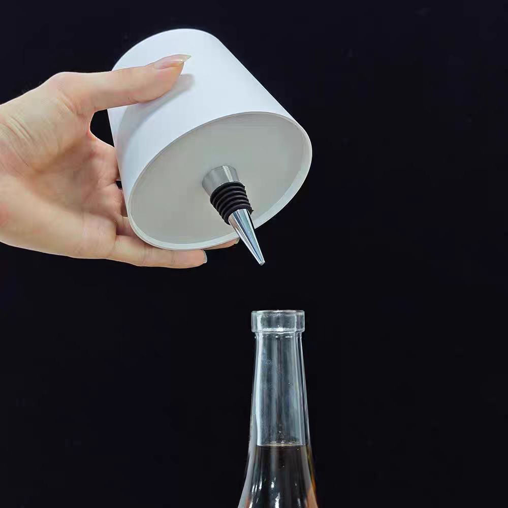 Hand holding a white bottle cap with a metal valve over a glass bottle on a black background