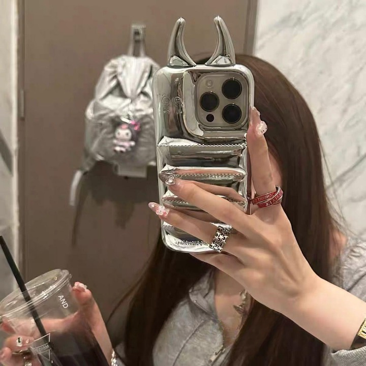 Person holding a phone with a unique case, wearing rings, in front of a mirror.