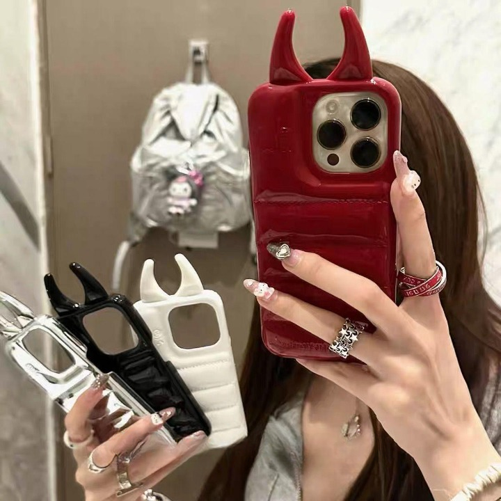 Person holding a red phone case with devil horns, black and white phone cases in the background.