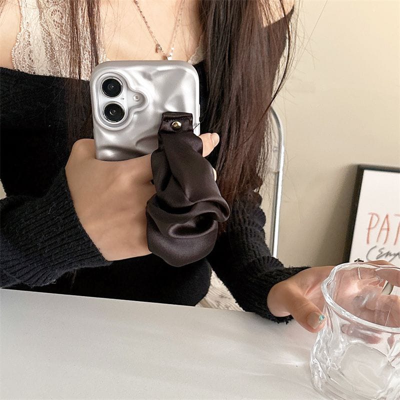 Person holding a phone with a reflective case, wearing a dark sweater and brown gloves.