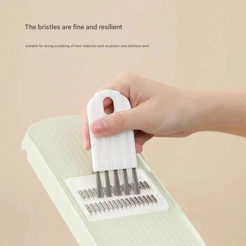Hand holding a white brush with metal bristles over a green scrubber on a beige background.