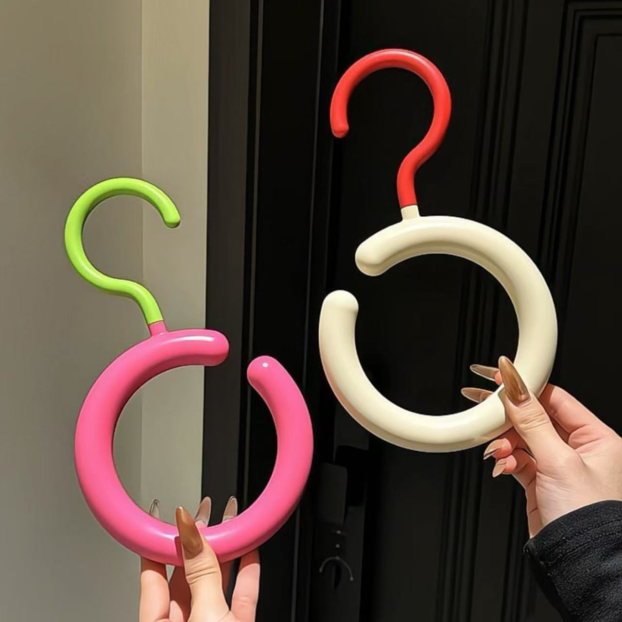 Colorful hooks held by hands against a black door.