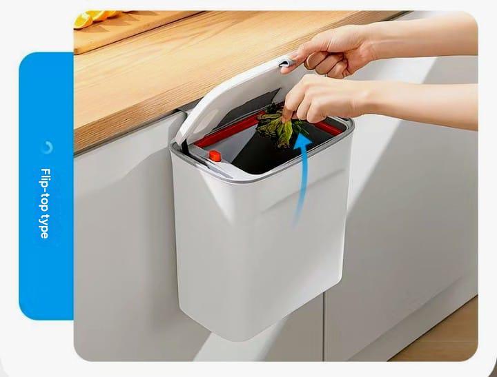 Person disposing of waste into a white trash can with a flip-top lid on a wooden surface.