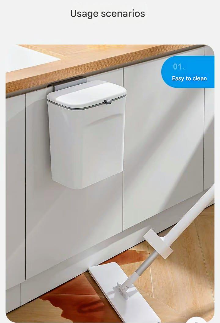 Wall-mounted trash can next to a kitchen cabinet with a mop on the floor.