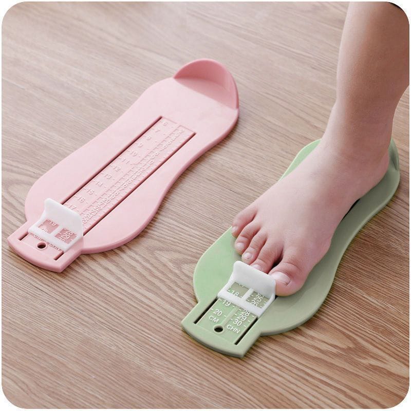 Pink and green foot measuring devices on a wooden surface with a child's foot stepping on the green device.