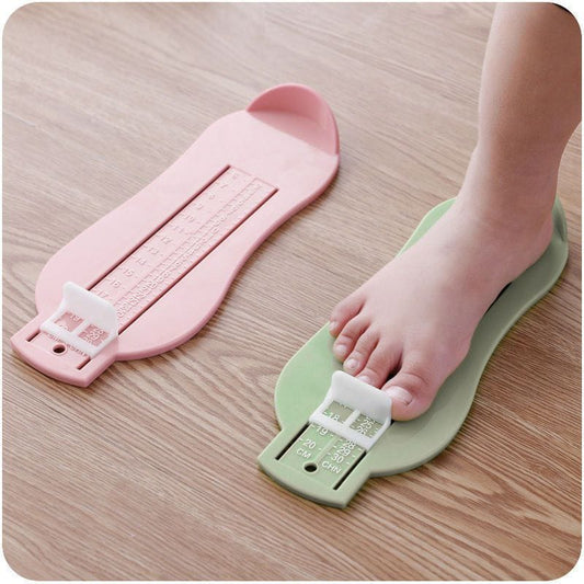 Pink and green foot measuring devices on a wooden surface with a child's foot stepping on the green device.