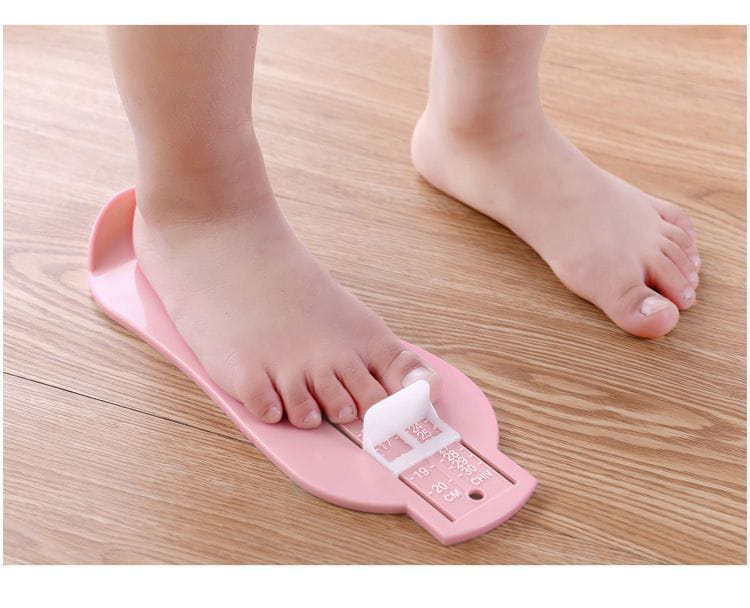 Pink foot measuring device on a child's foot with wooden floor background