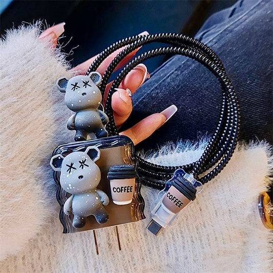 Coiled black USB cable with bear and coffee cup charms on a textured surface