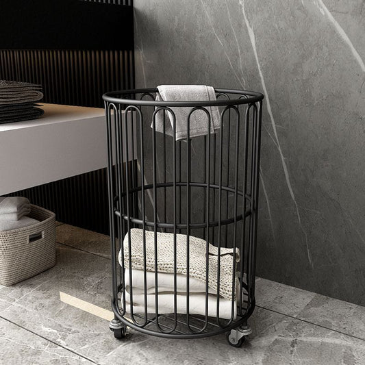 Black metal laundry basket with clothes inside on a tiled floor.